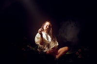 a woman sitting in a dark room holding a cigarette